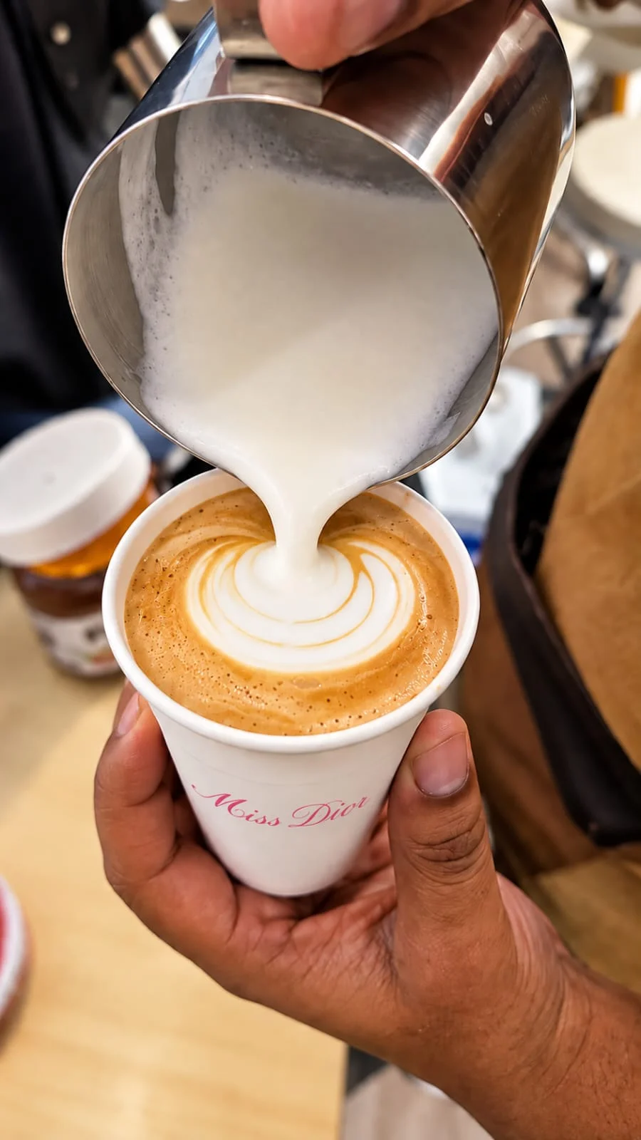 Barista preparando latte art em um café personalizado para Miss Dior